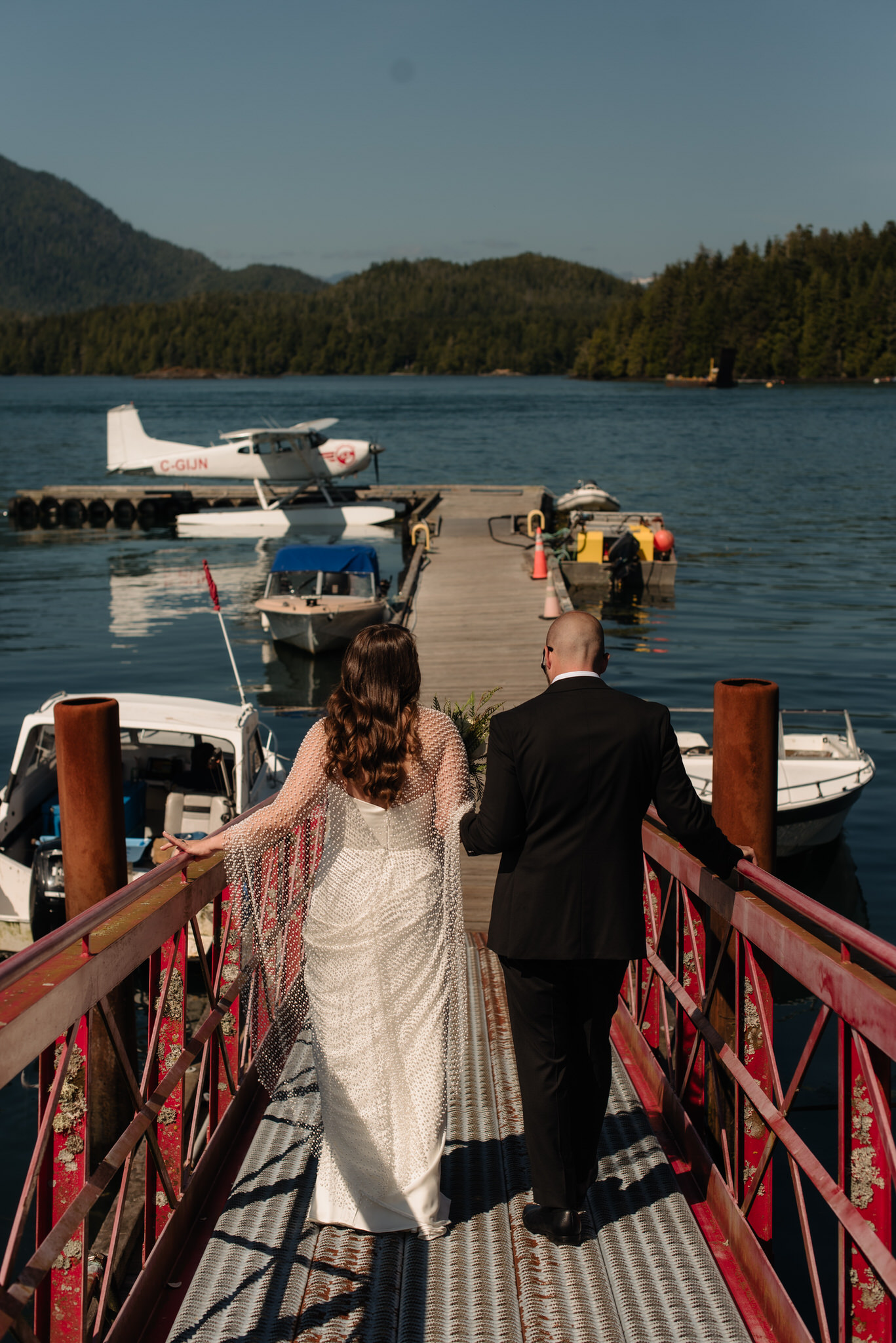 The bride and groom walk down a dock in downtown Tofino